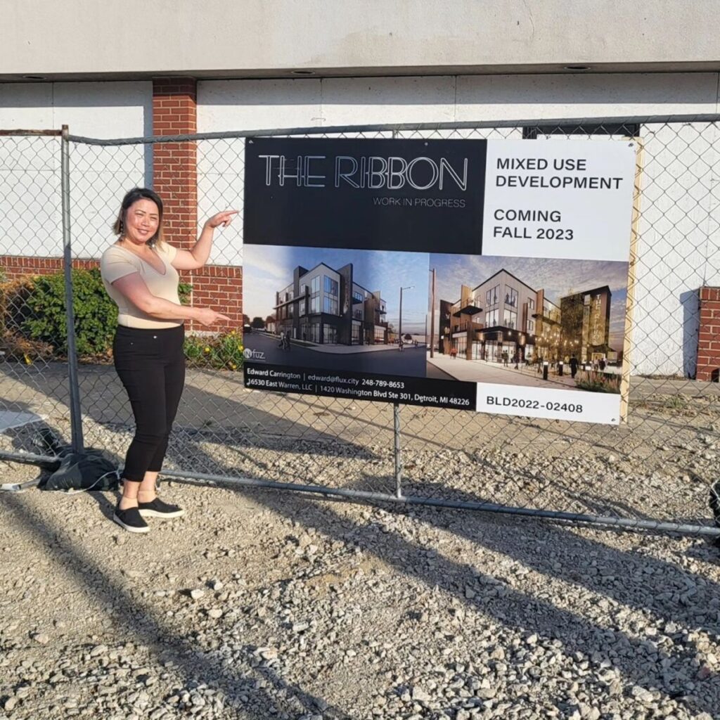 gajiza dumplins owner standing next to the ribbon in detroit construction site sign